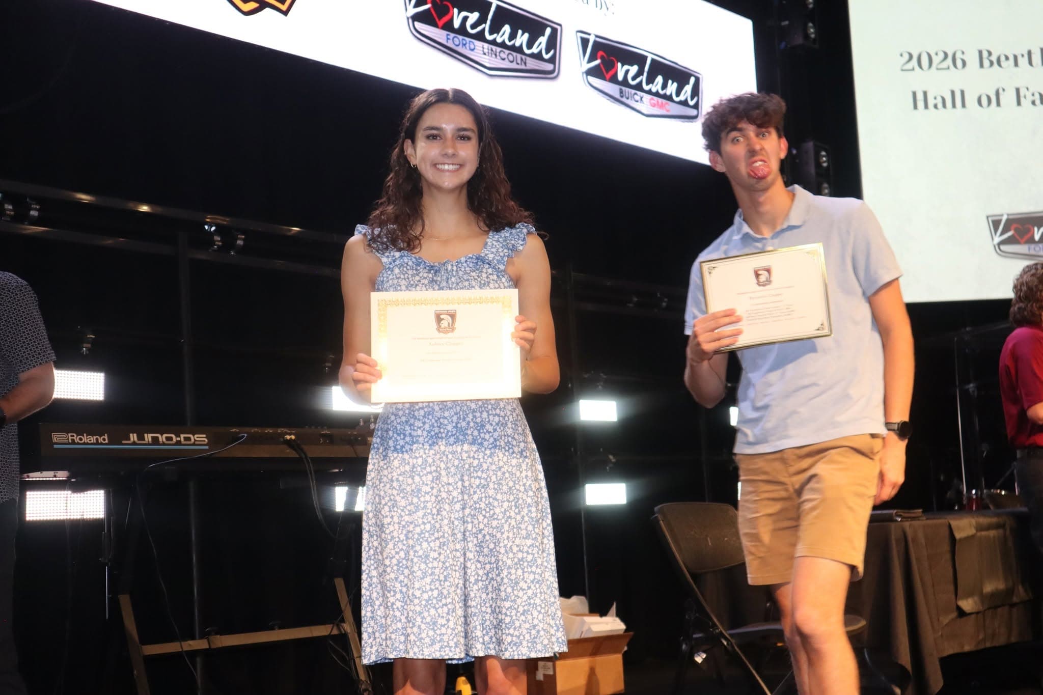 Two young people on stage holding certificates in front of Berthoud branding